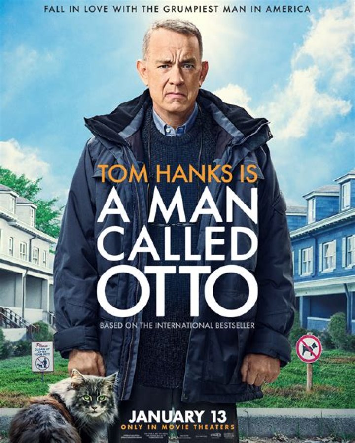 Otto (Tom Hanks) bends over to detach the claws of a pretty limp-looking CG cat that&rsquo;s lying on its stomach on the ground of his garage, with its paws hooked into his pant cuff, in A Man Called Otto